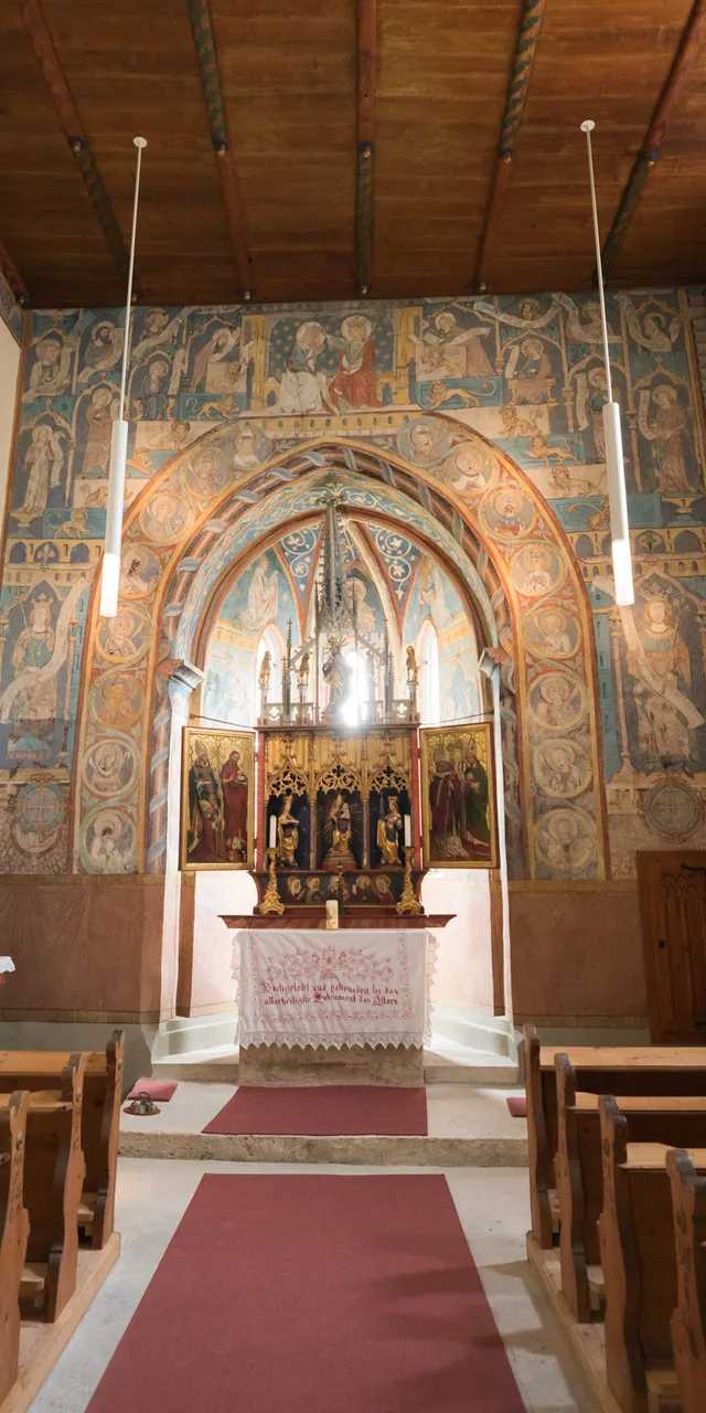 Innenraum einer kleinen historischen Kirche mit Holzbankreihen, Wandmalereien und verziertem Altar